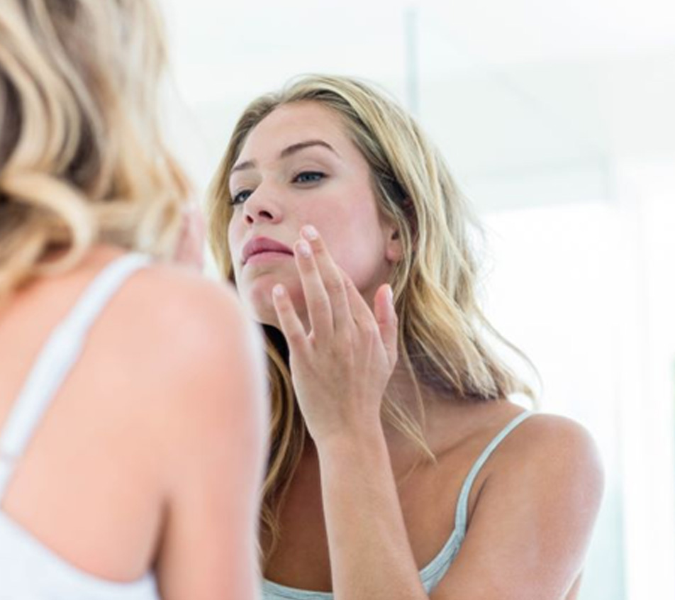 Woman looking at herself in mirror, concerned about signs of aging